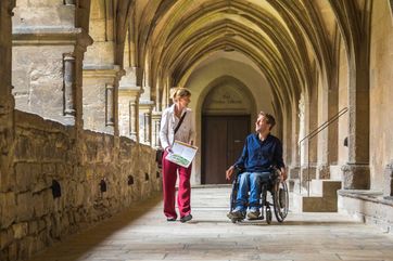 Rollstuhlfahrer und eine Frau als Begleitperson im Kreuzgang des Naumburger Doms
