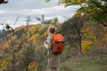 Unterwegs auf der SaaleHorizontale rund um die Universitätsstadt Jena: Der Qualitätsweg eröffnet immer wieder besondere Ausblicke, wie hier über die herbstlich gefärbten Wälder von Ziegenhain hinüber zum Fuchsturm, dem markanten Bergfried der ehemaligen Burg Kirchberg. Foto: Thüringer Tourismusverband Saale-Holzland e. V., Falko Matte